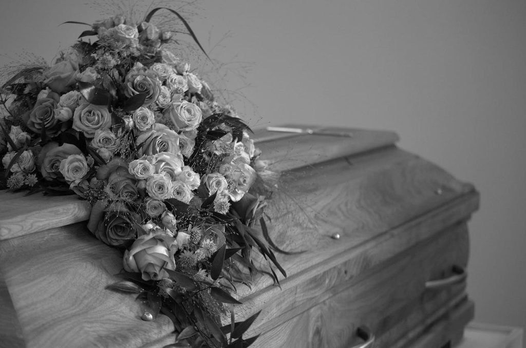 A black and white image featuring a wooden casket adorned with a vibrant floral bouquet, symbolizing respect and memory.