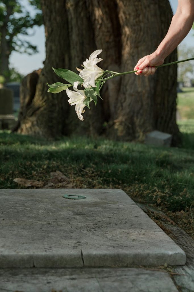 A hand holding white lilies over a grave, symbolizing mourning and remembrance.