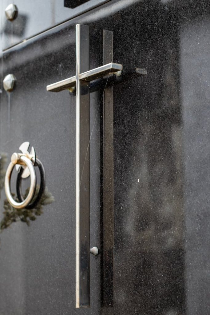 A detailed view of a steel cross on a dark mausoleum door, symbolizing Christianity.