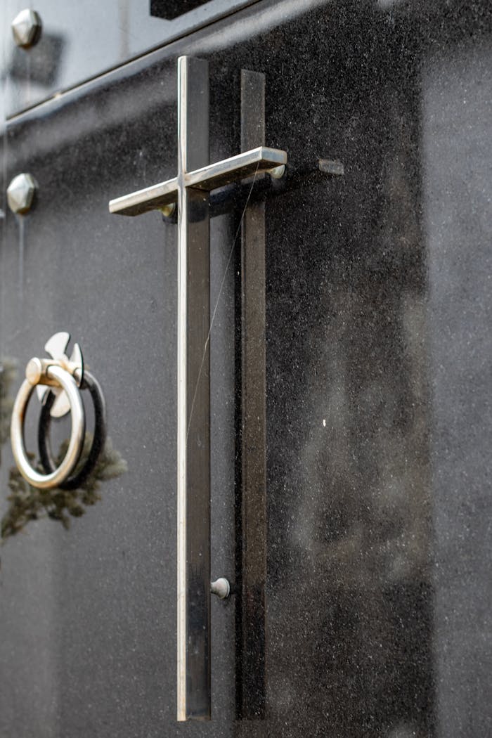 A detailed view of a steel cross on a dark mausoleum door, symbolizing Christianity.